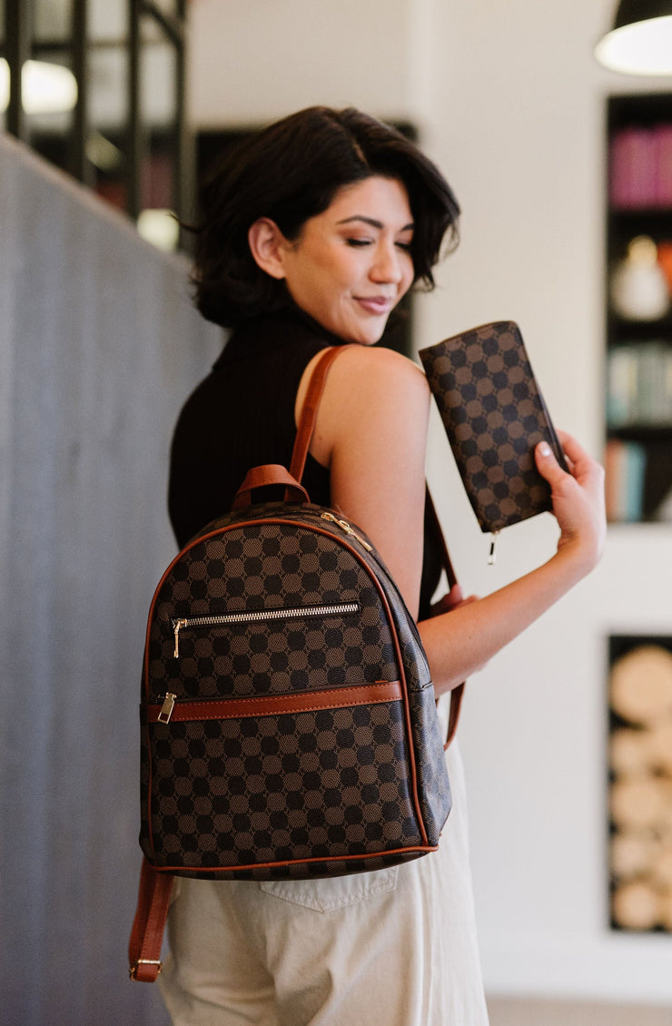 woman carrying a vegan leather dome backpack on one shoulder and holding a matching wallet