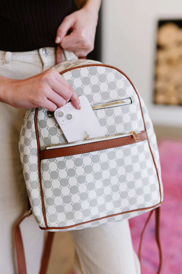 a black and white circle patterned backpack with contrasting brown trim. a phone is being slid inside the front pocket.