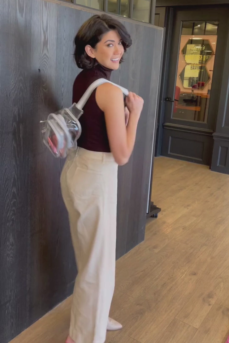 Woman modeling a clear sling bag with silver trim and unzipping pockets